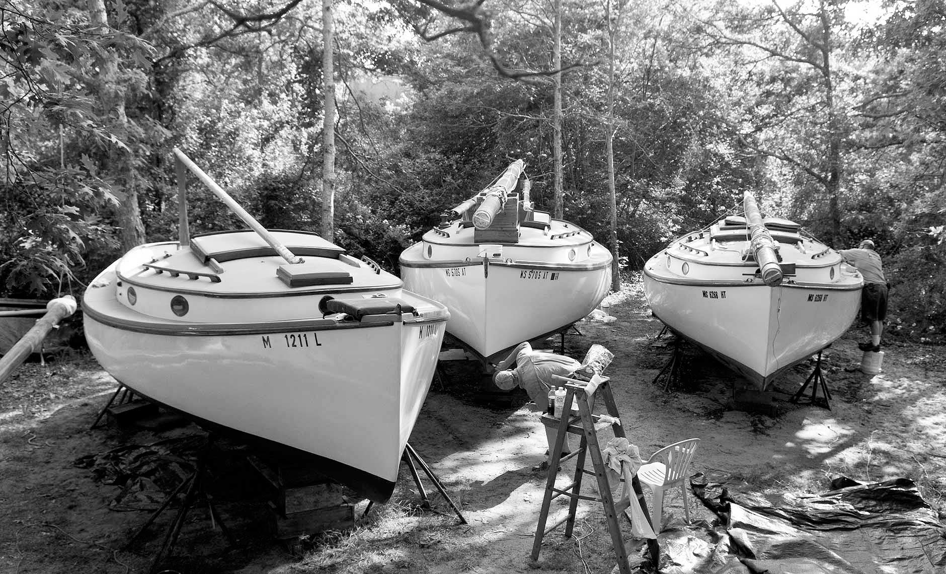 Black and white photograph of 3 catboats in boatyard